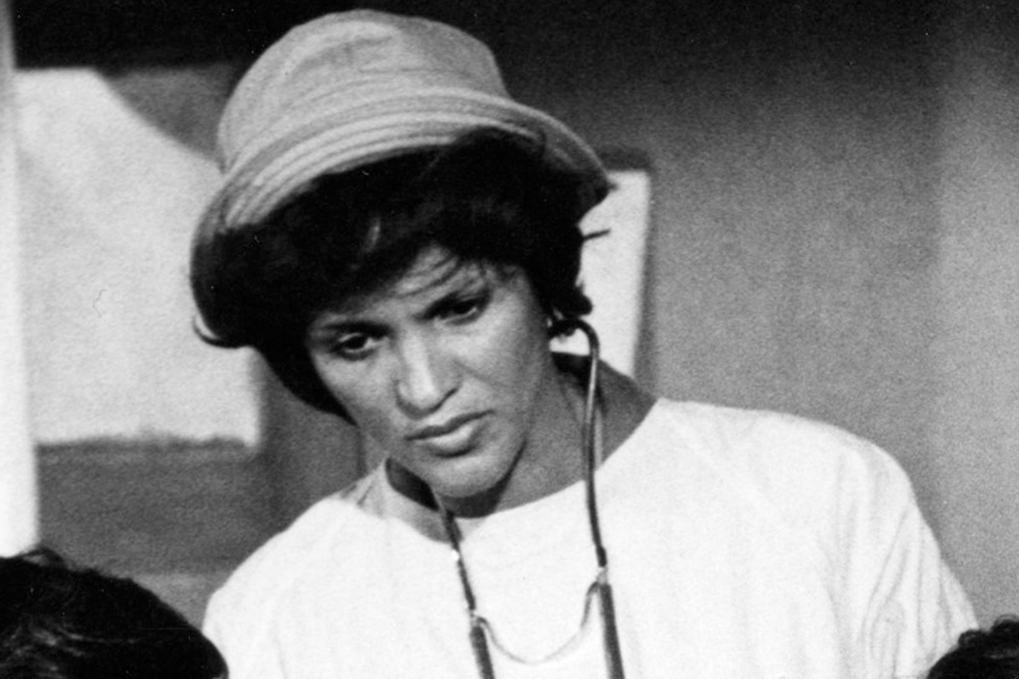 Black and white photo of a woman in a bucket hat and stethoscope around her neck, looking down and to the left.