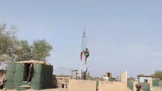 A militant climbs up a tower with a flag at at what appears to be a military base with barricades and makeshift container buildings, in Tessalit, Mali, in this screen grab obtained from a social media video released on May 1, 2026. SOCIAL MEDIA/via REUTERS