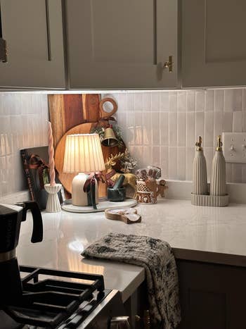 Cozy kitchen corner with lamp, decorative cutting boards, festive decor, and modern soap dispensers on white countertop