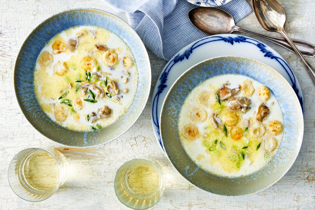 Two bowls of Simple Oyster Stew on a table with spoons, a napkin, and glasses of white wine.