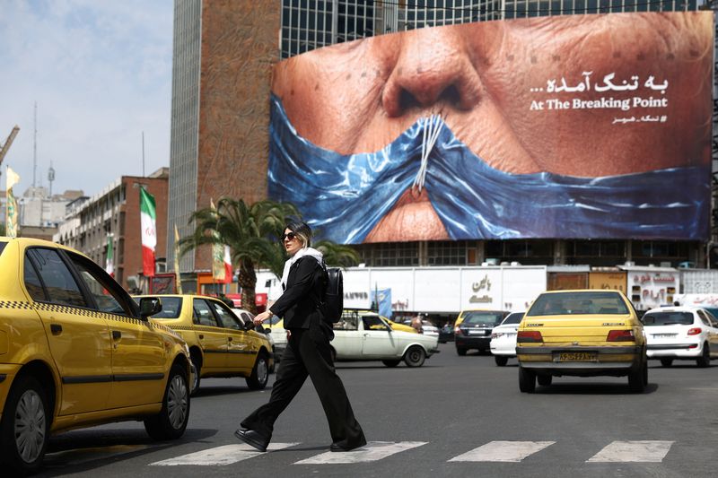 Woman walks past anti-U.S. billboard depicting U.S. President Donald Trump and the Strait of Hormuz, in Tehran