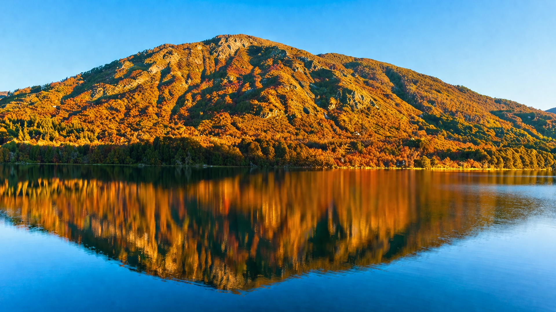 Un lago como un espejo que refleja las montañas otoñales al atardecer