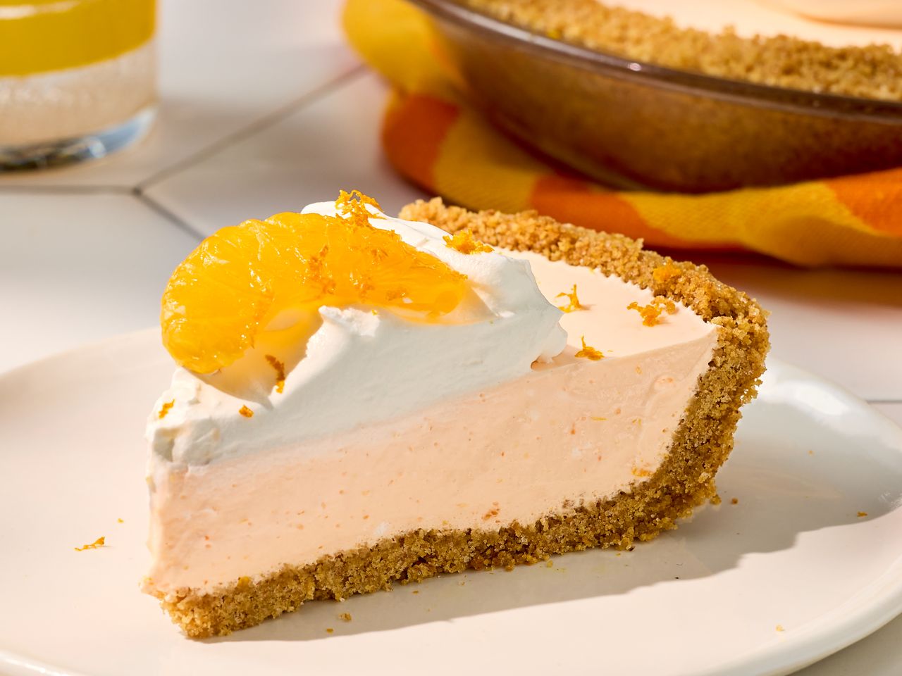 Slice of cream pie topped with whipped cream and an orange slice, set on a white plate