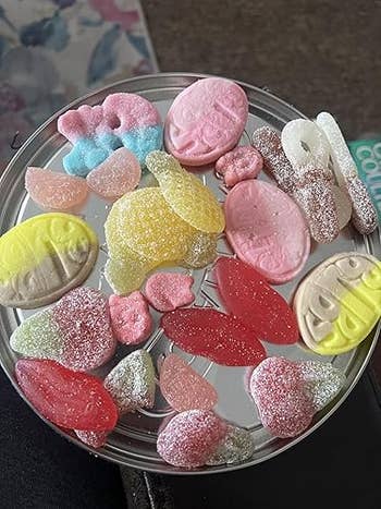 Assorted gummy candies and sour sweets displayed on a round metal tray