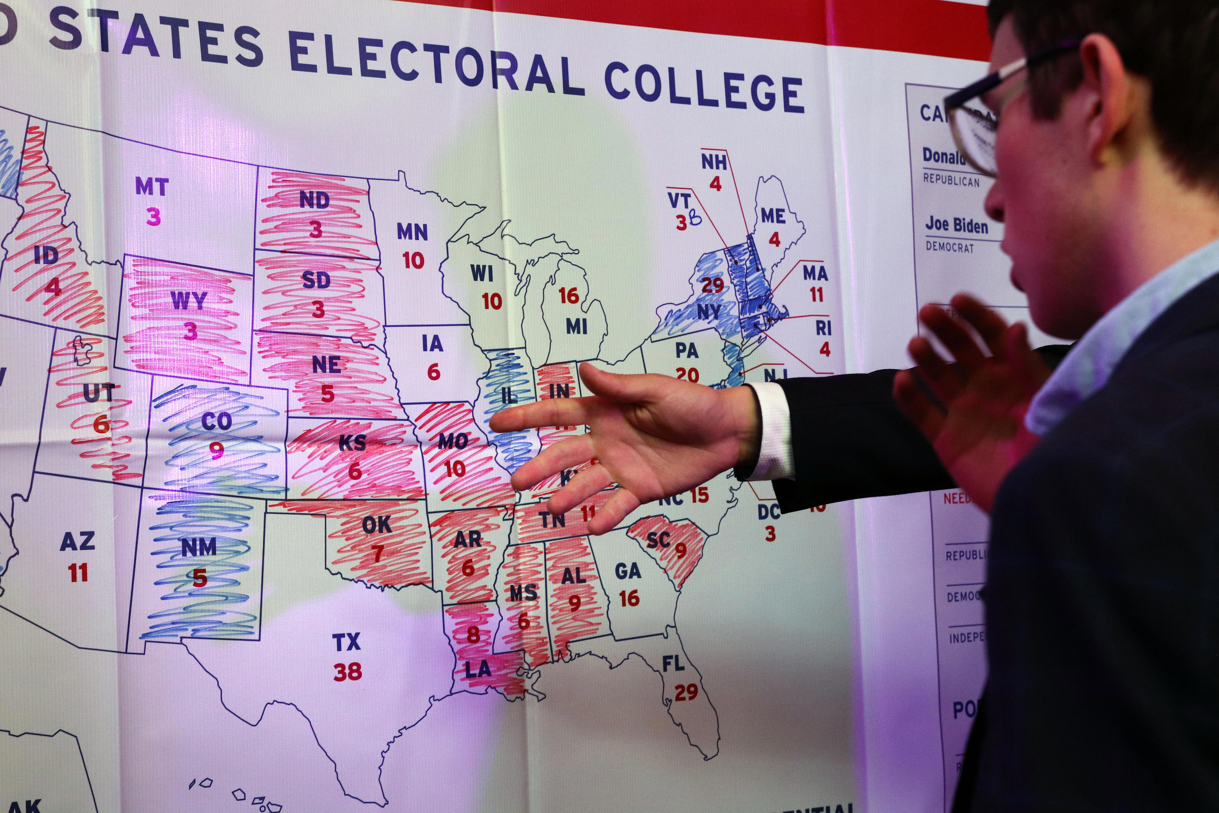 Picture of a map of the electoral college with states colored in for each candidate, as a person points to it