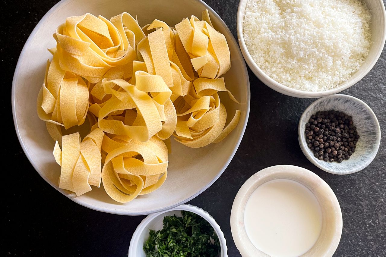 Ingredients arranged for preparing Cacio e Pepe including pasta grated cheese cream black pepper and herbs