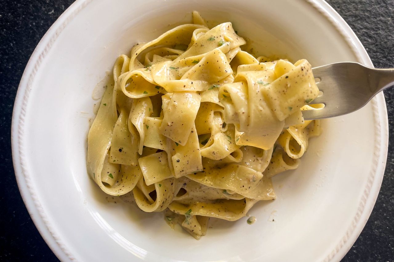 A plate of pappardelle pasta with a fork featuring a creamy cacio e pepe sauce