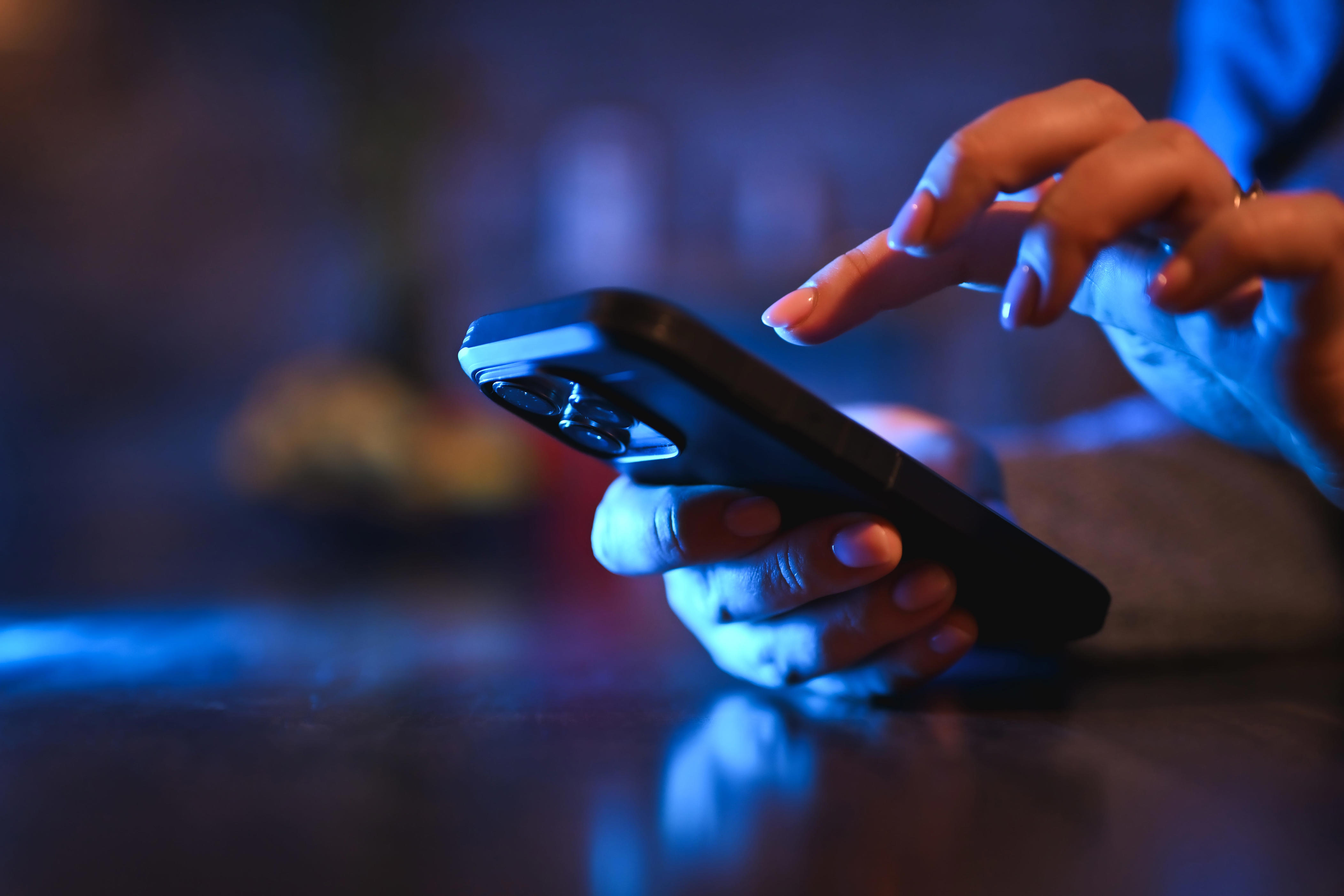 Woman's hands texting on a mobile phone with blue screen light in a dark room