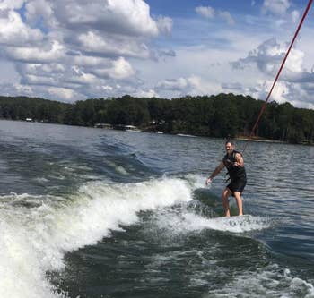 Person wakeboarding on a lake, holding a rope, with trees and a cloudy sky in the background