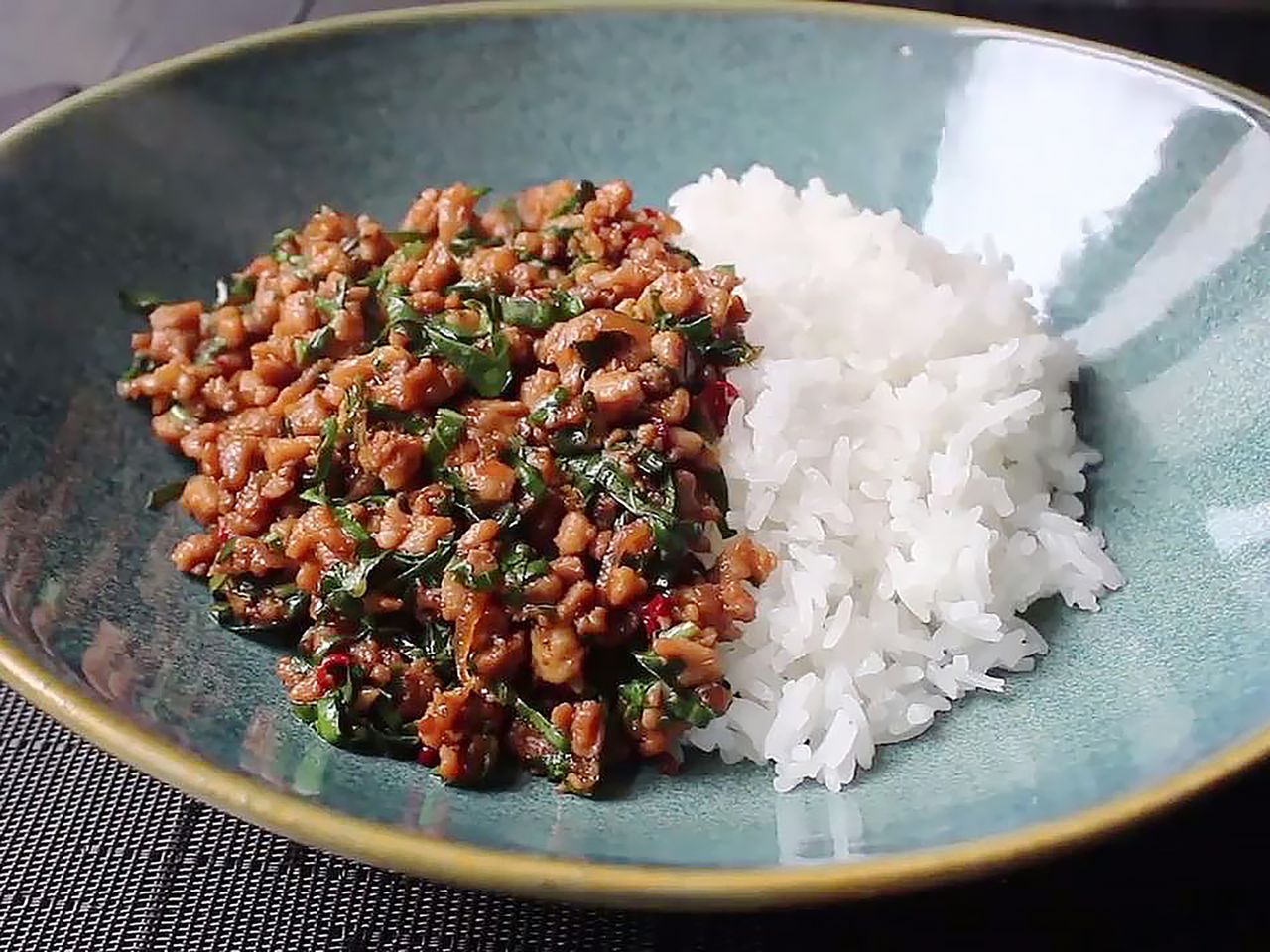a mid angle view looking into a bowl of spicy thai basil chicken served next to steamed white rice.