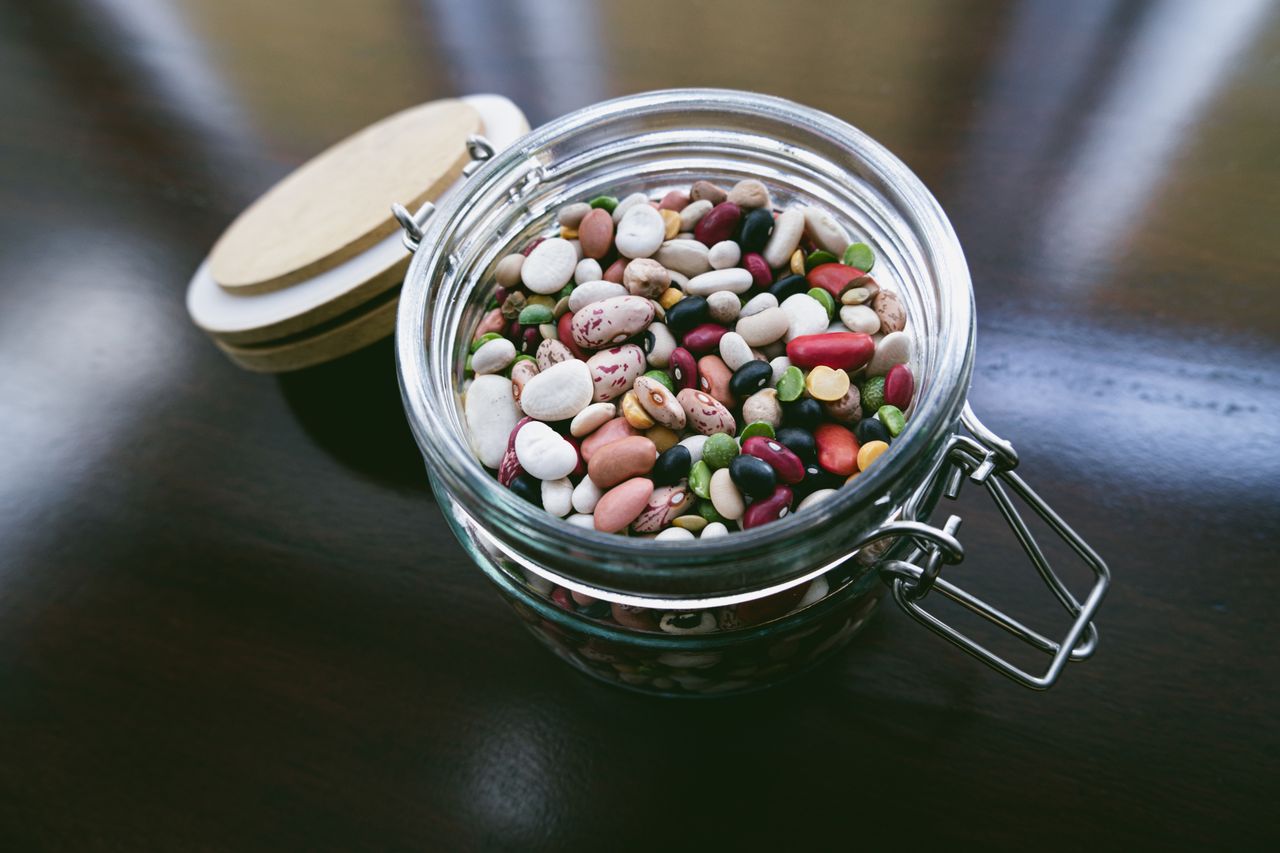 A jar filled with assorted beans on a wooden surface