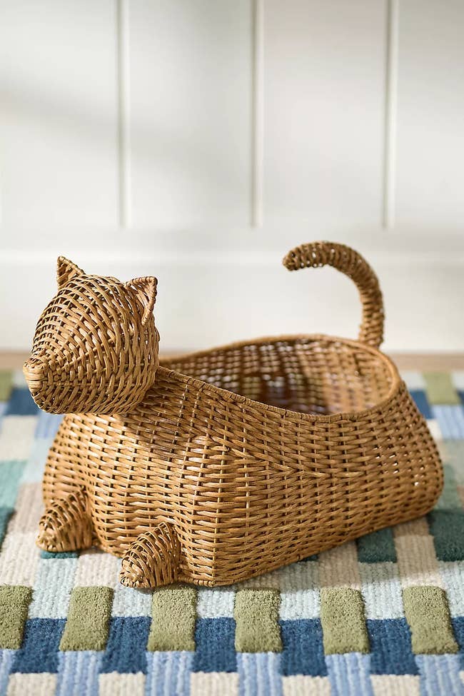 Wicker basket shaped like a cat with a curved tail, displayed on a patterned rug. Ideal for home decor or storage