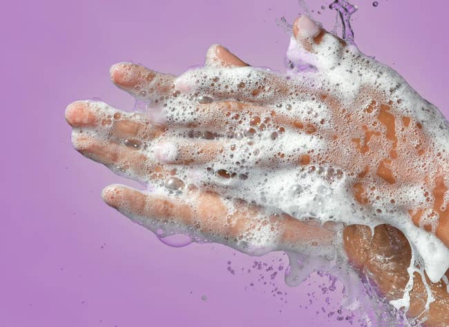 Hands covered in foaming soap against a plain backdrop with text reading