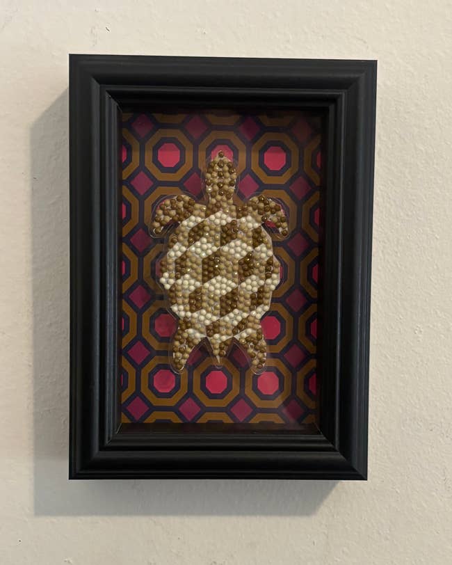 Framed beaded turtle artwork on geometric patterned background, suitable for home décor