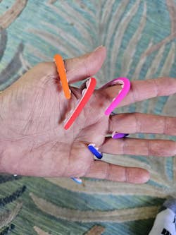 A hand displaying several colorful hair ties looped around the fingers on a patterned fabric background