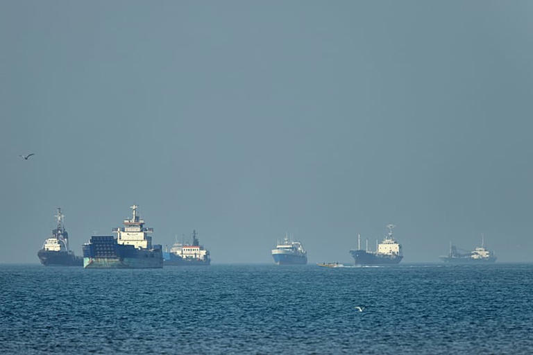 Navi da carico all'ancora al largo mentre un piccolo motoscafo passa in primo piano, nello Stretto di Hormuz al largo di Bandar Abbas, in Iran, lunedì 4 maggio 2026. Amirhosein Khorgooi/ISNA via AP
