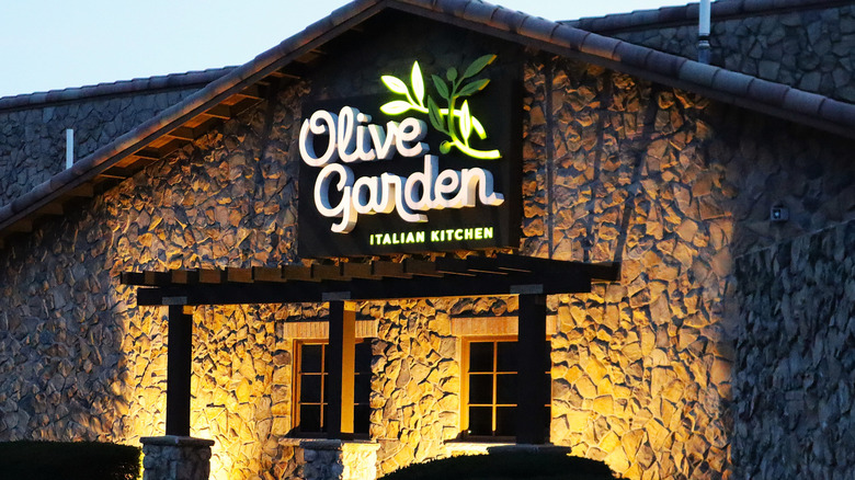 The exterior of an Olive Garden restaurant with an illuminated sign glowing in the twilight