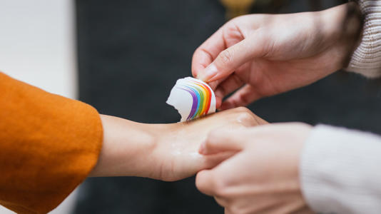 Close-up of person applying temporary rainbow tattoo to hand