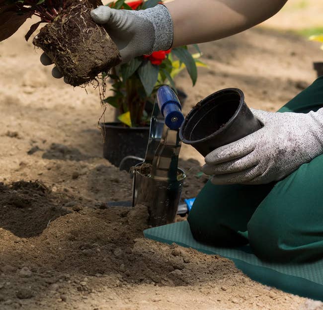 A person kneeling on the green mat while gardening