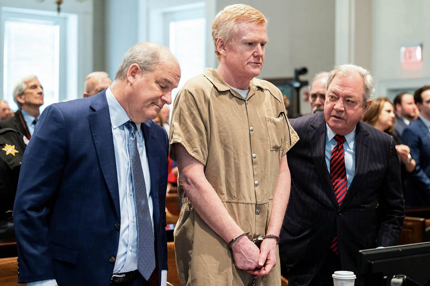Alex Murdaugh stands handcuffed between two lawyers in a courtroom.
