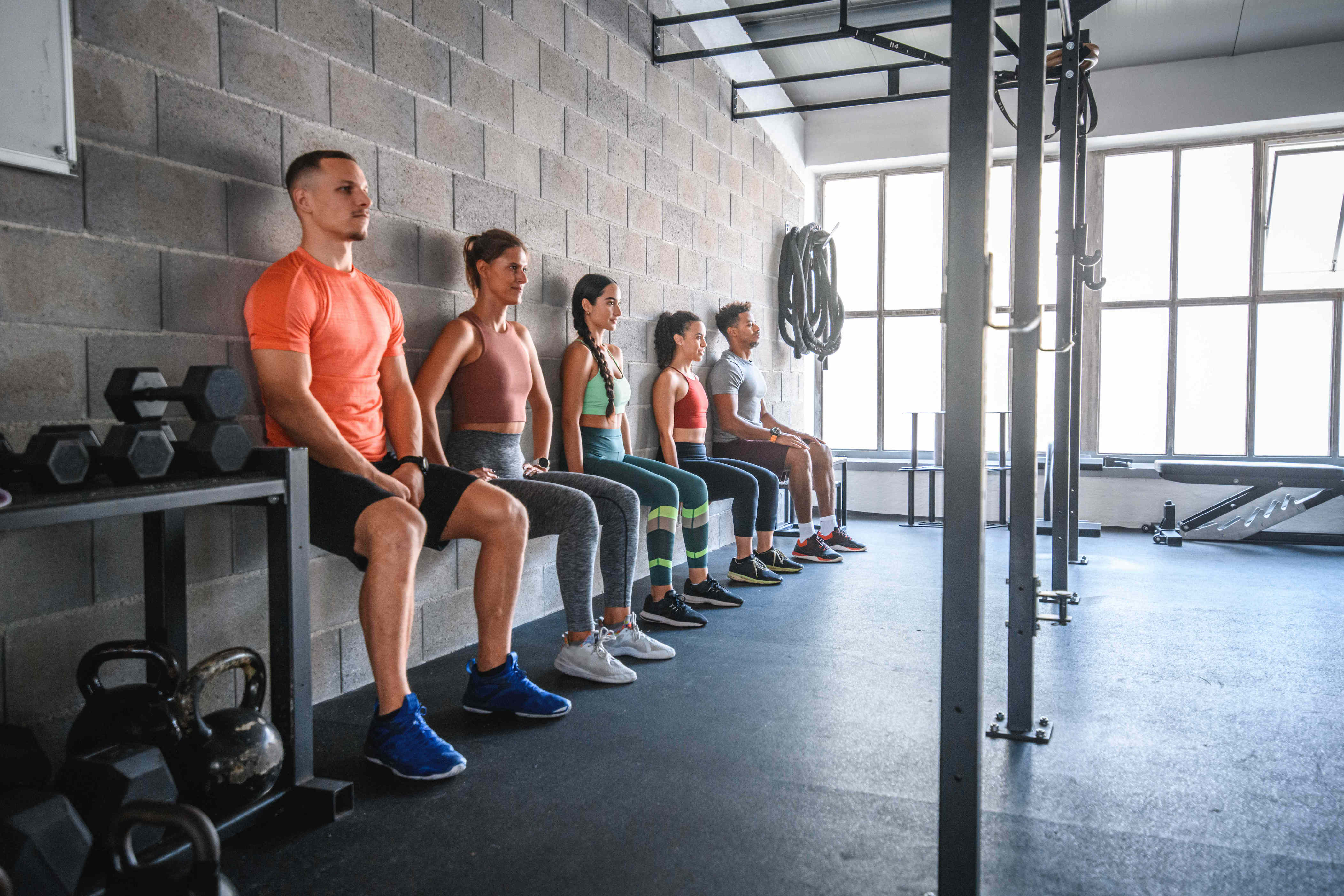 People sitting against a gym wall performing wall sit exercises