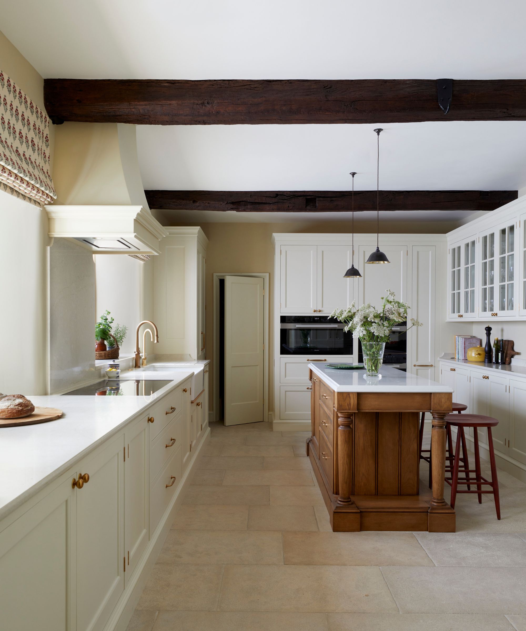 A country kitchen with white cabinets, a wood island, and stone flooring