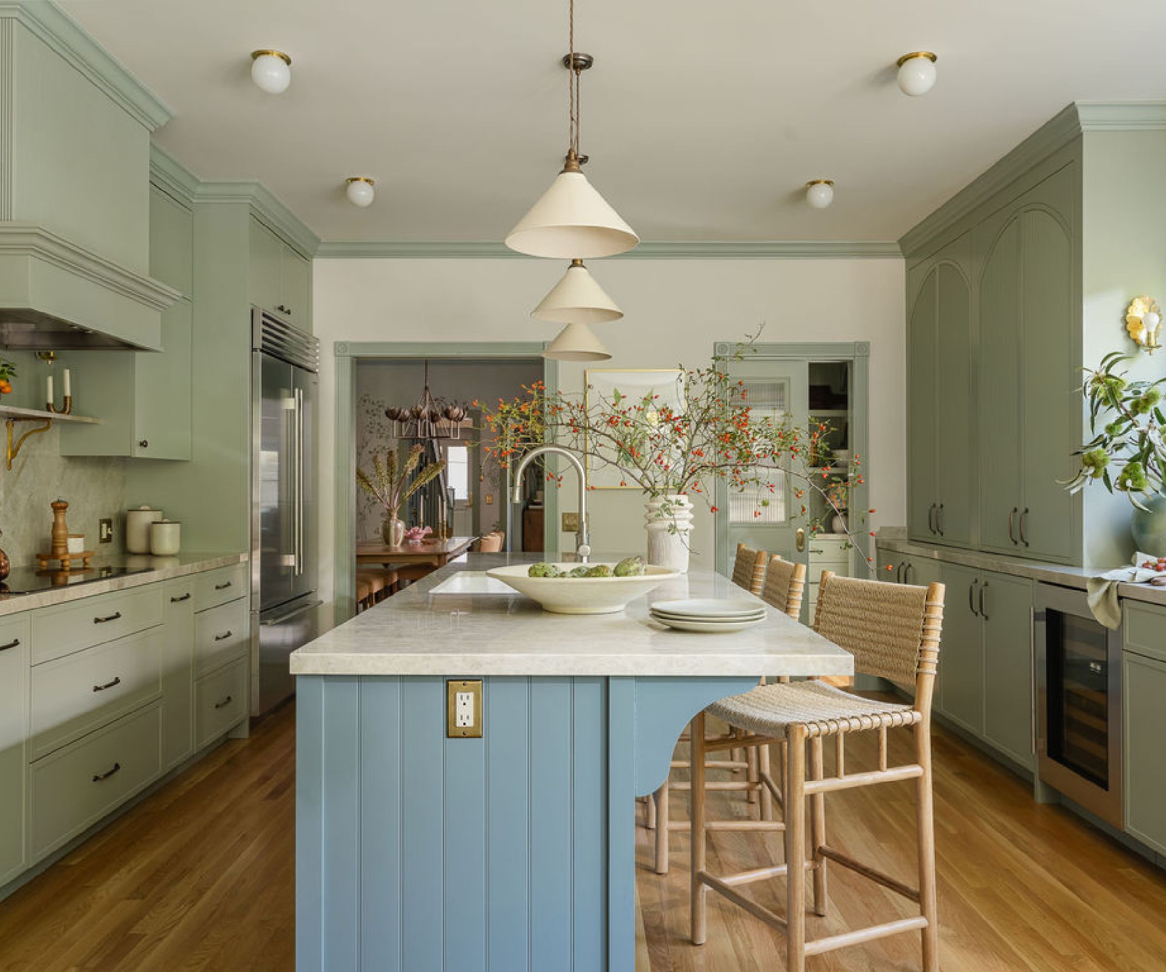 A green kitchen with a blue island, white walls, and trim painted the same green as the units