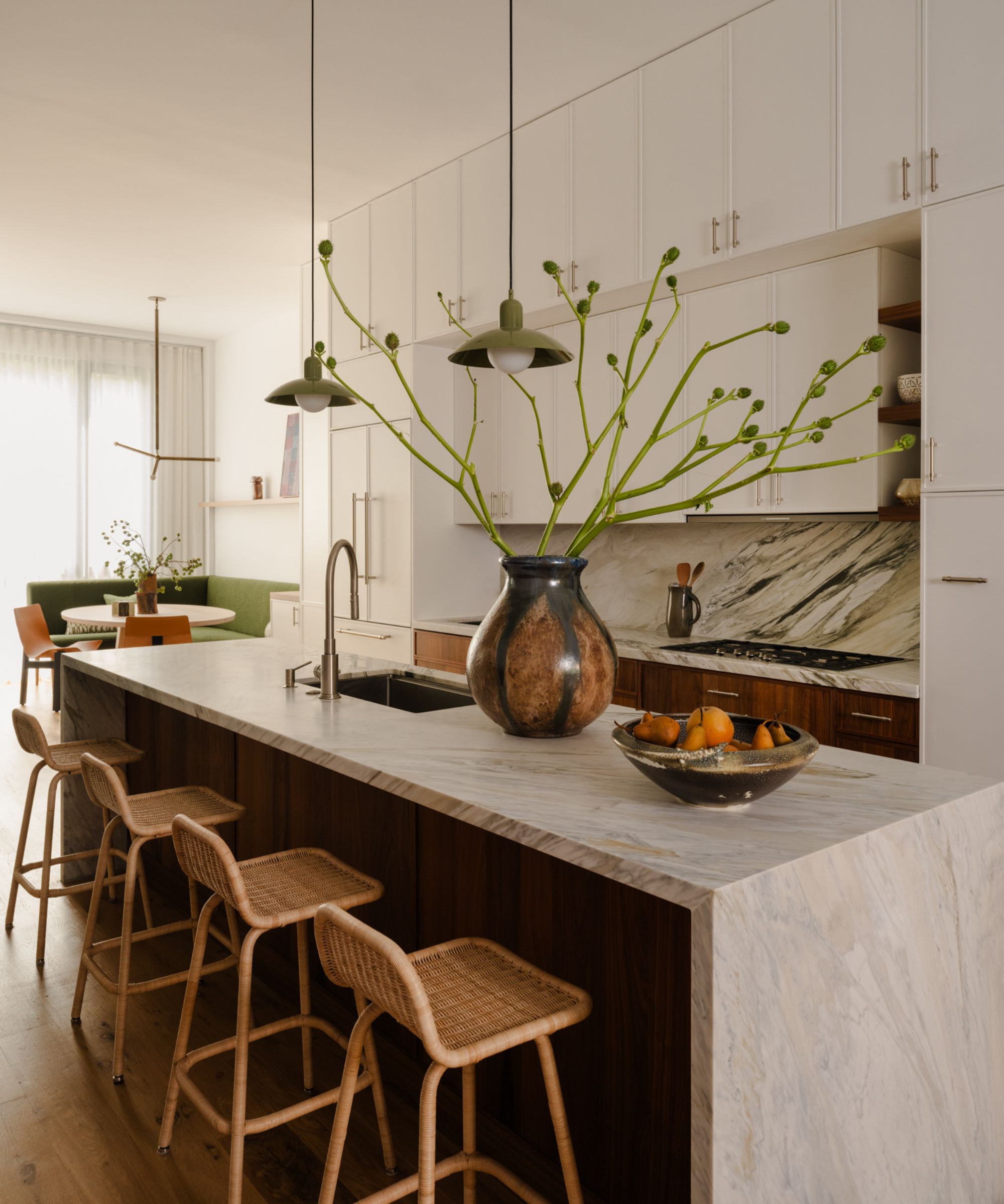 A white kitchen with a stone waterfall countertop over the island and green accesnts through decor