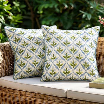 Two decorative throw pillows with a leafy pattern on a wicker outdoor sofa