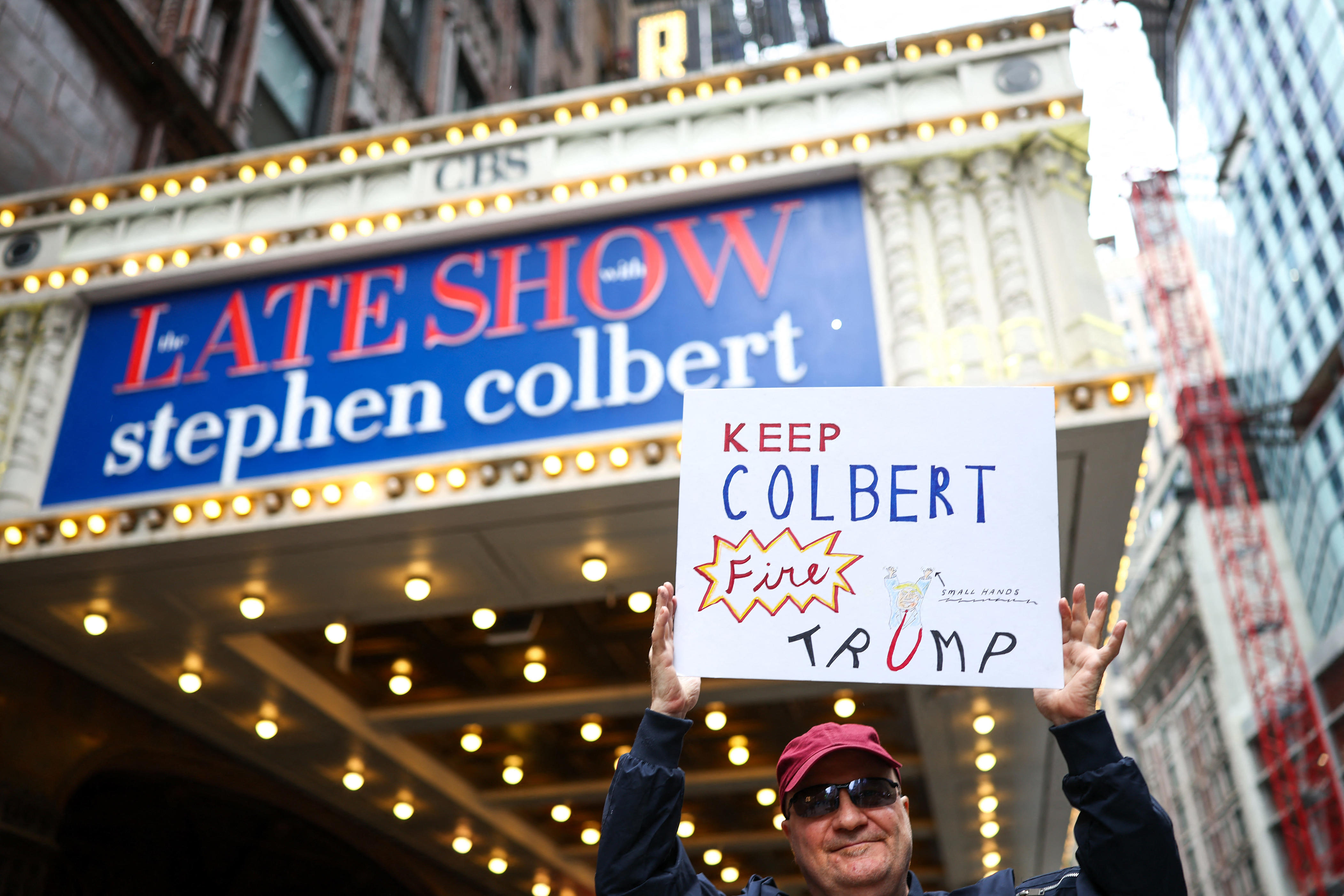 A man holds a sign outside the Ed Sullivan Theater ahead of the taping of the final episode of the "The Late Show" in New York, on May 21, 2026. "The Late Show" frontman Stephen Colbert will host the final edition of the 33-year-old US cultural institution on May 21, after it was cancelled by CBS as the network courted President Donald Trump. The show, which Colbert has hosted since 2015, was axed after he mocked the broadcaster for a $16 million settlement with Trump for allegedly "maliciously" editing an interview with his Democratic election rival Kamala Harris.