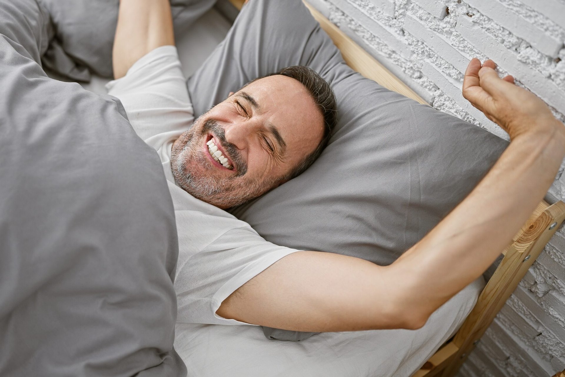 Smiling middle-aged man in bed, waking up happy and well-rested after a good night's sleep.