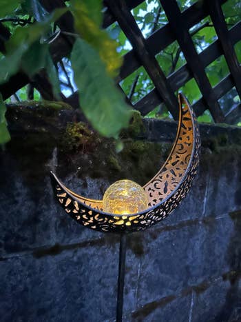 Decorative garden solar light shaped like a crescent moon with filigree pattern glowing in low light