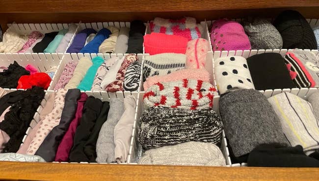 Drawer neatly organized with various socks rolled in sections, including patterns, solids, and textures, ideal for decluttering and efficient storage