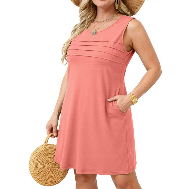 Person wearing a sleeveless, casual knee-length dress with layered pleats, accessorized with a straw hat and bag, suitable for summer outings