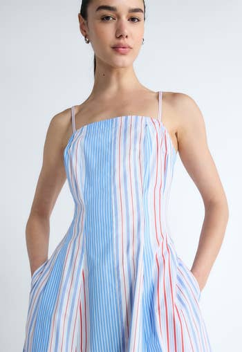 Person wearing a sleeveless, striped sundress with thin straps and pockets, posing hands in pockets