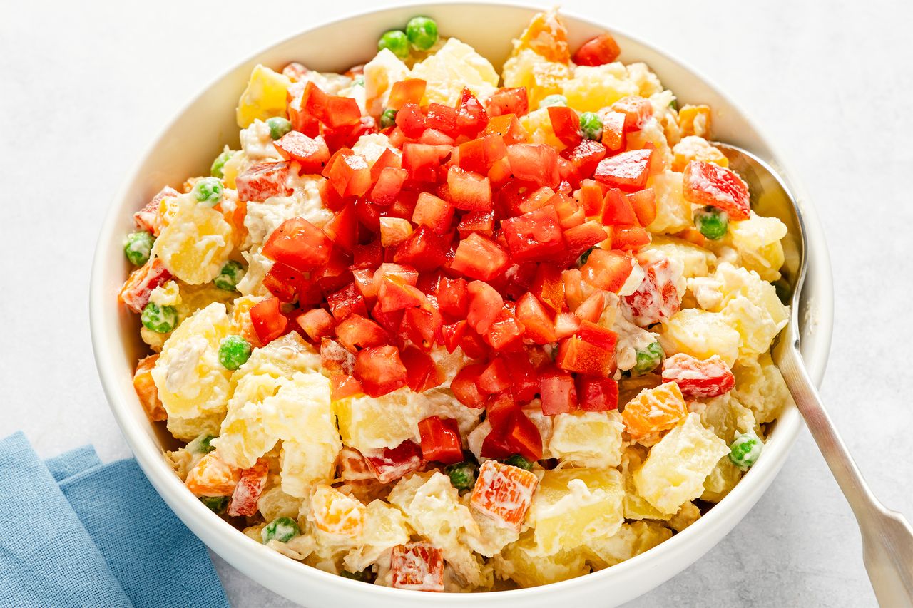 A bowl of potato salad with diced tomato garnish on top containing peas carrots and creamy dressing