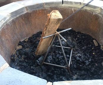 Vertical fire pit log holder with charred wood and ash inside a stone fire pit. Ideal for controlled burning and efficient heat distribution