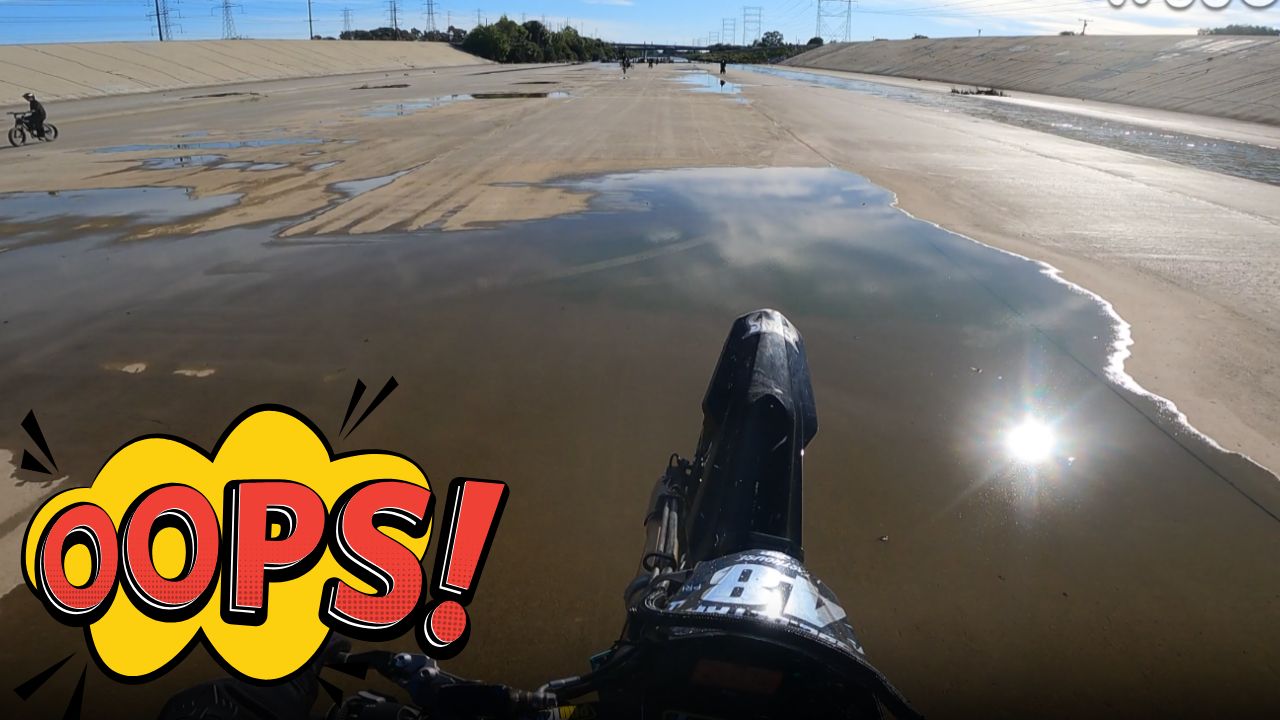 Electric dirt bike rider falls after slipping in wet riverbed