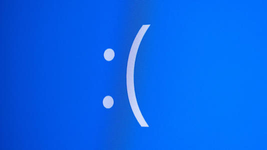 Close-up of a blue computer error screen displaying a large white sad-face emoticon, commonly associated with the Windows "Blue Screen of Death."