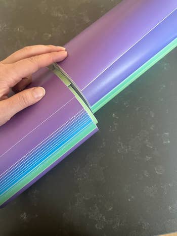 Person holding a multi-gradient colored large folder with several sections and documents inside, suitable for organizing or office use
