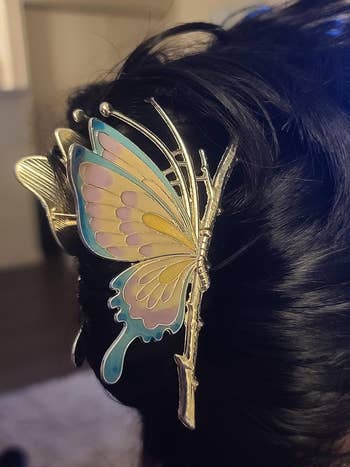 A metallic butterfly hair clip with intricate wing design adorns styled dark hair