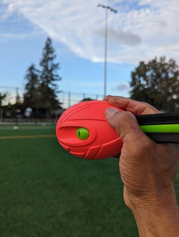 Hand holding a fitness tool outdoors on a sports field with trees and a light pole in the background