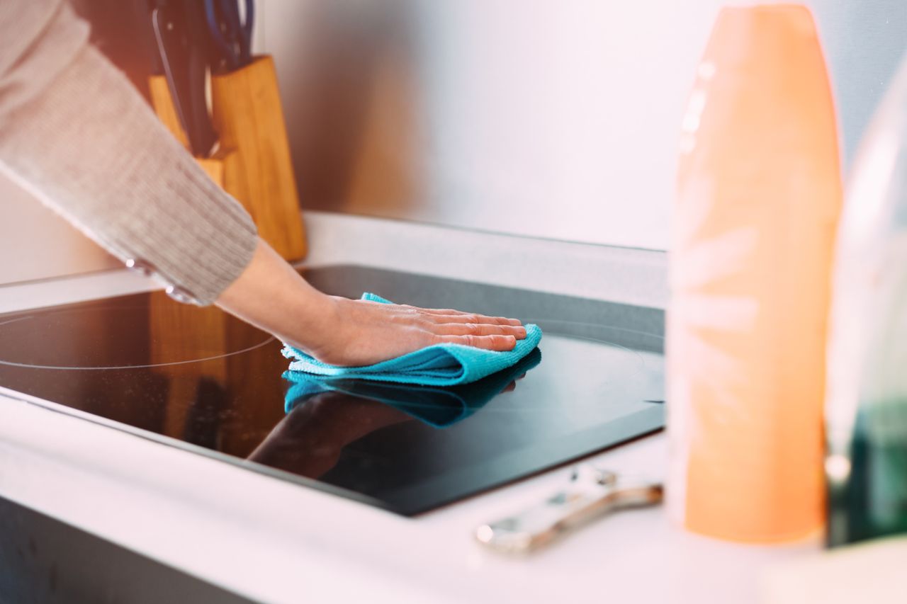 A person cleaning a stovetop with a cloth in a kitchen setting