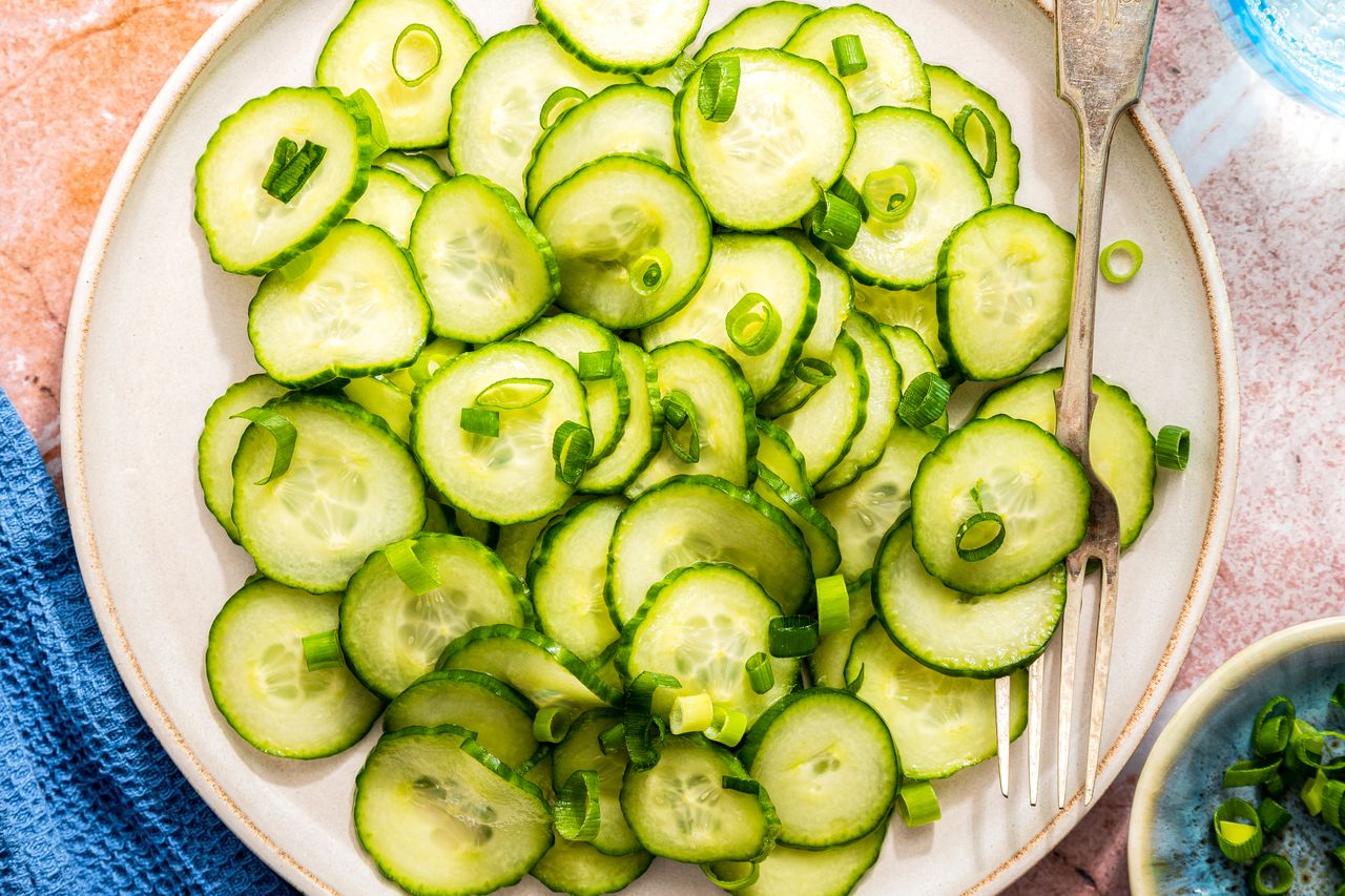 Plate of cucumber salad with sliced cucumbers and green onions served with a fork