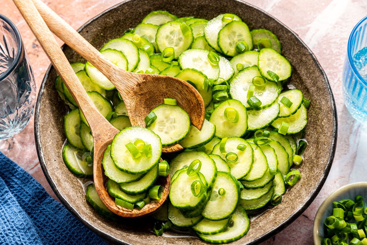 A bowl of sliced cucumber salad with green onions served with wooden utensils
