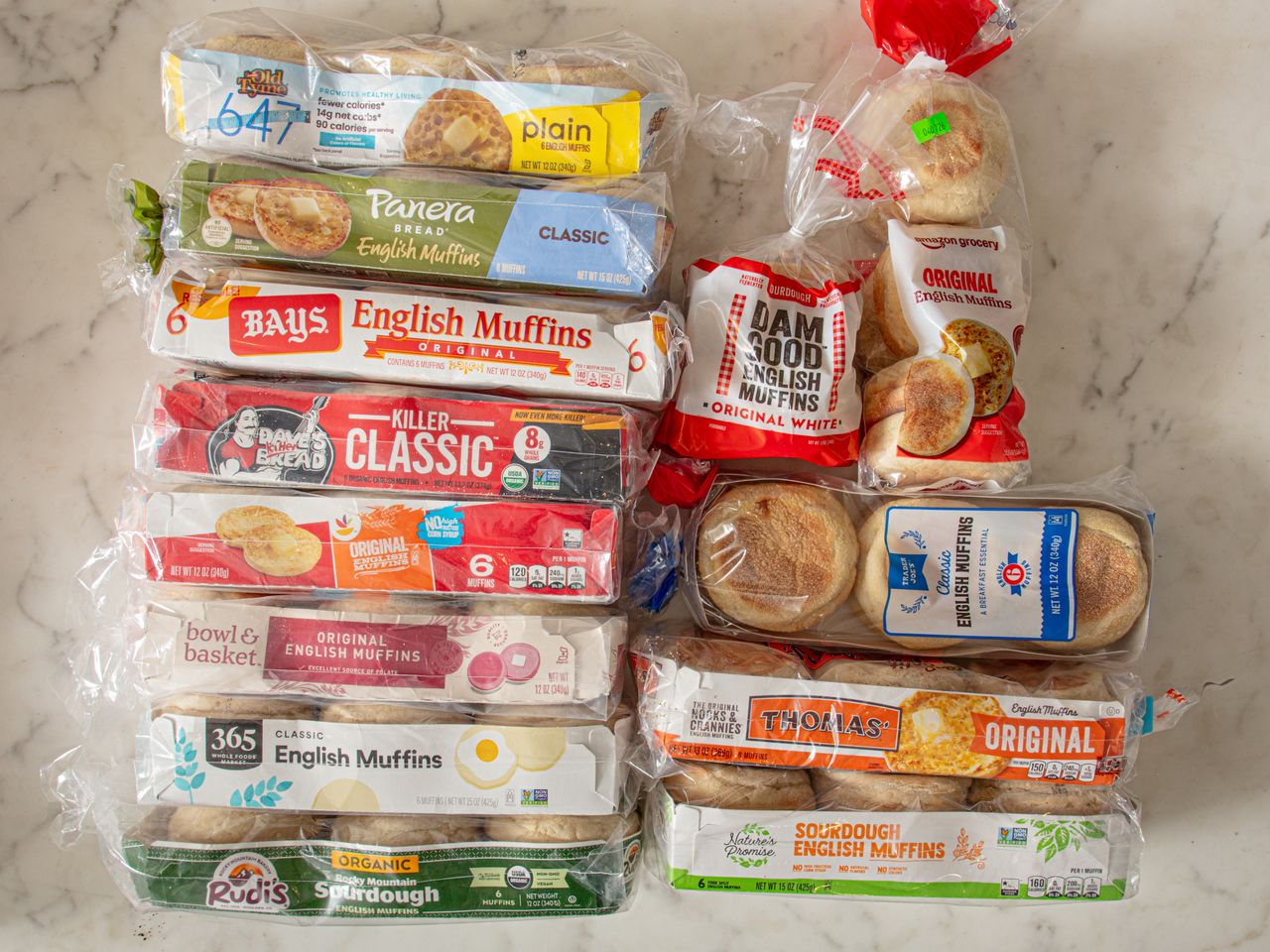 Various brands of packaged English muffins arranged on a surface
