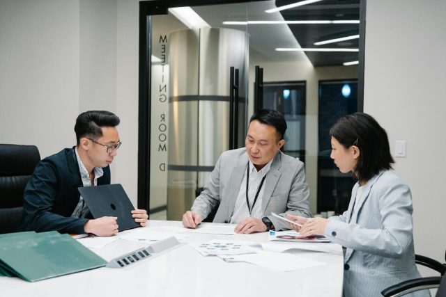 Business meeting with three professionals collaborating in a modern conference room setting.