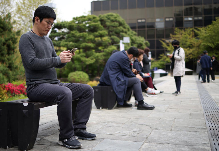 Office workers look at their mobile phones during a lunch break in Seoul. Photo: Reuters