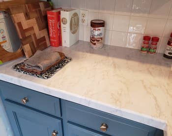 Marble-style kitchen countertop with books, a tin of chocolate, and spices. Two folded towels are placed on a dish rack