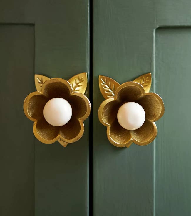 Decorative floral cabinet knobs with petal details and central round handles, adding elegance to green paneled doors. Ideal for home decor shopping